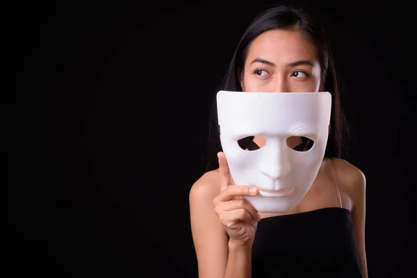 Faccia di giovane bella donna asiatica pensando mentre tiene maschera — Foto Stock