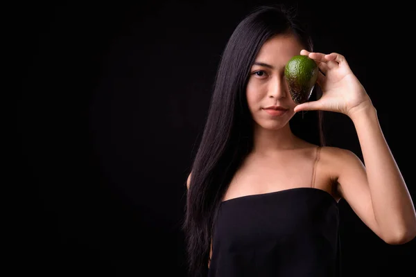 Porträtt av ung asiatisk kvinna som håller avokado nära ansiktet — Stockfoto