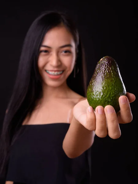 Portrait of happy young beautiful Asian woman holding avocado — Stock Photo, Image