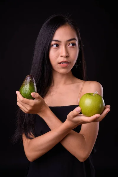 Portrait of young Asian woman thinking with apple and avocado — Stock Photo, Image
