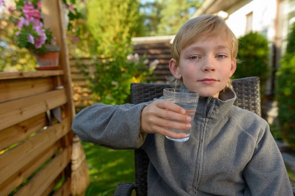 Mladý pohledný chlapec se sklenicí vody sedí na dvorku — Stock fotografie
