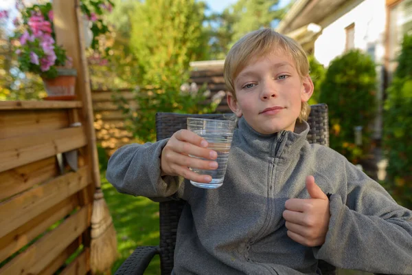 Młody przystojny chłopiec z szklanką wody dając kciuki w górę w podwórku — Zdjęcie stockowe