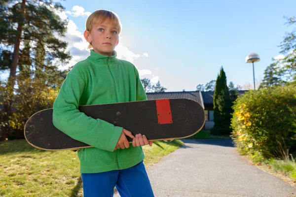 Mladý hezký chlapec myšlení při držení skateboard v přední dvoře — Stock fotografie