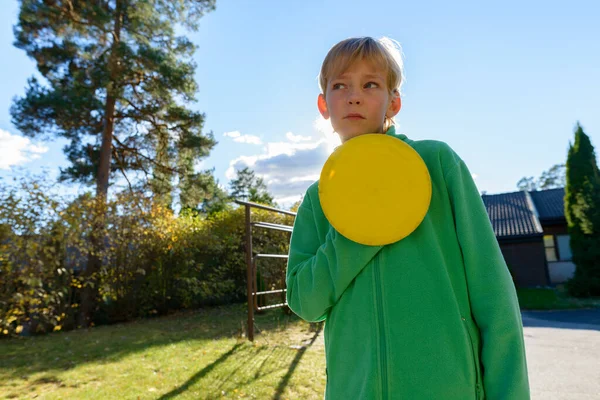 Mladý pohledný chlapec myšlení při držení frisbee v přední zahradě — Stock fotografie