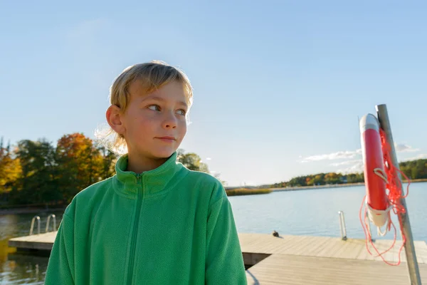 Młody przystojny chłopiec myśli na drewnianym molo w pobliżu rzeki — Zdjęcie stockowe