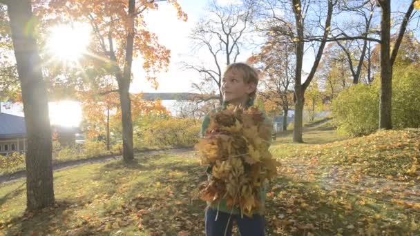 Glad ung stilig pojke kastar höstlöv på parken — Stockvideo