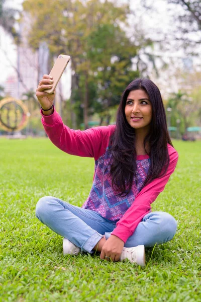 Portrait of young beautiful Persian woman relaxing at the park