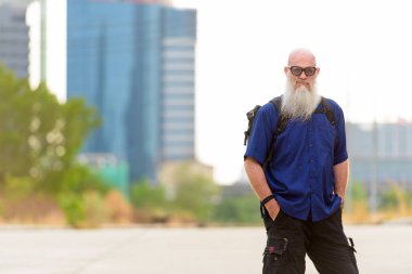 Portrait of mature handsome bald tourist man with long beard in the streets outdoors