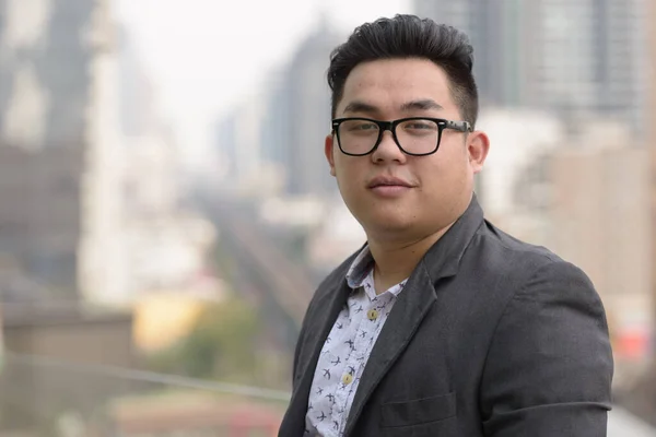 Portrait of young handsome overweight Filipino businessman in suit against view of the city