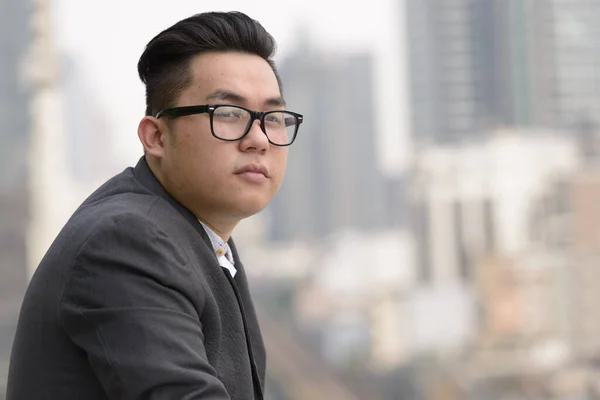 Portrait of young handsome overweight Filipino businessman in suit against view of the city