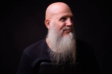 Studio shot of mature bald bearded man against black background