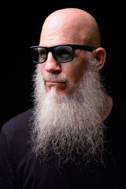 Studio shot of mature bald bearded man against black background