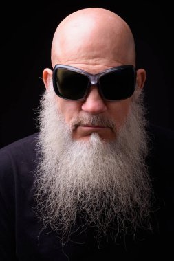 Studio shot of mature bald bearded man against black background