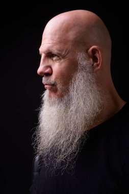 Studio shot of mature bald bearded man against black background