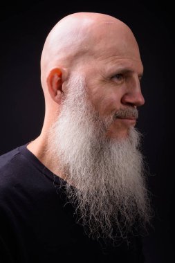 Studio shot of mature bald bearded man against black background