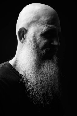 Studio shot of mature bald bearded man against black background in black and white