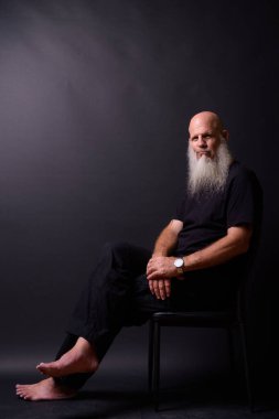 Studio shot of mature bald bearded man against black background