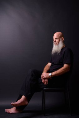 Studio shot of mature bald bearded man against black background