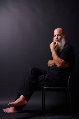 Studio shot of mature bald bearded man against black background