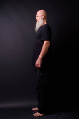 Studio shot of mature bald bearded man against black background