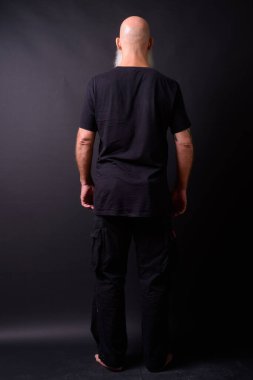 Studio shot of mature bald bearded man against black background