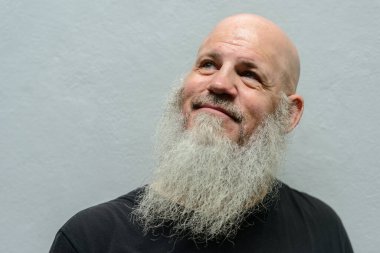 Portrait of mature handsome bald hipster man with long beard against concrete wall