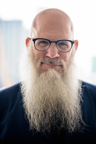 Portrait of mature handsome bald hipster businessman with long beard against view of the city