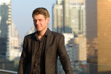 Portrait of young handsome businessman in suit against view of the city