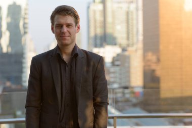 Portrait of young handsome businessman in suit against view of the city