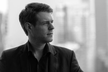 Portrait of young handsome businessman in suit against view of the city in black and white