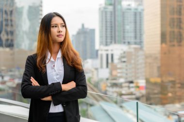 Portrait of young beautiful Asian businesswoman against view of the city