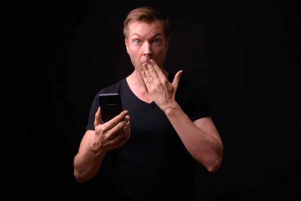 Portrét mladého pohledného muže pomocí telefonu a vypadá šokovaně — Stock fotografie