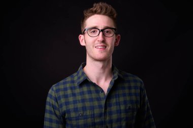 Studio shot of young handsome hipster man with eyeglasses against black background