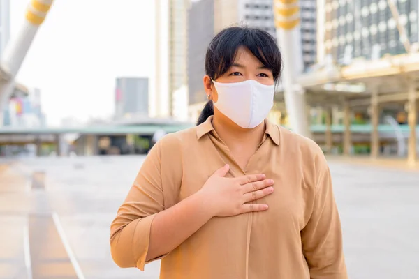 Portrait of overweight Asian woman with mask for protection from corona virus outbreak at skywalk bridge in the city