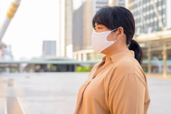 Portrait of overweight Asian woman with mask for protection from corona virus outbreak at skywalk bridge in the city