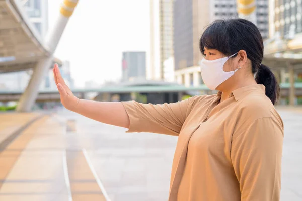 Portrait of overweight Asian woman with mask for protection from corona virus outbreak at skywalk bridge in the city