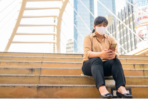 Portrait of overweight Asian woman with mask for protection from corona virus outbreak at skywalk bridge in the city
