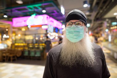 Korona virüsü salgınından korunmak için maske takan yetişkin sakallı bir hipsterin portresi.