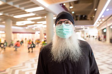 Korona virüsü salgınından korunmak için maske takan olgun sakallı turist portresi.