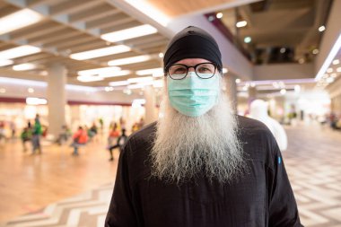 Korona virüsü salgınından korunmak için maske takan olgun sakallı turist portresi.