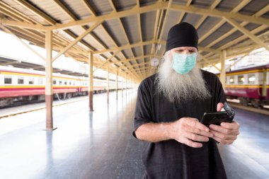 Tren istasyonundaki Corona virüsü salgınından korunmak için maskeli yetişkin sakallı hippi turist portresi.