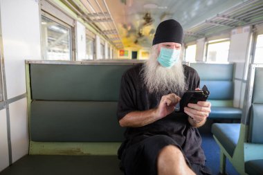 Korona virüsü salgınından korunmak için maske takan olgun sakallı turist portresi tren istasyonunda.