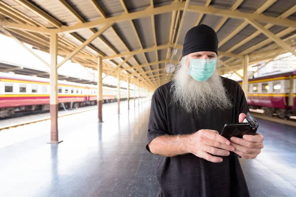 Tren istasyonundaki Corona virüsü salgınından korunmak için maskeli yetişkin sakallı hippi turist portresi.