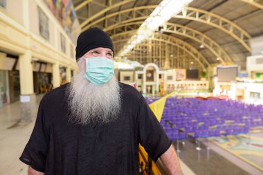 Korona virüsü salgınından korunmak için maske takan olgun sakallı turist portresi tren istasyonunda sosyal uzaklık