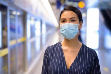 Metro istasyonunda Corona virüsü salgınından korunmak için maske takan Asyalı genç iş kadınının portresi.