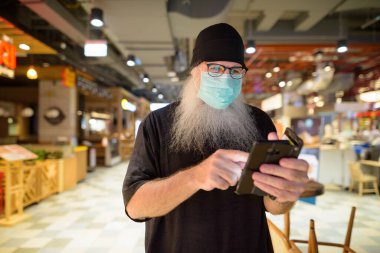 Korona virüsü salgınından korunmak için maske takan yetişkin sakallı bir hipsterin portresi.