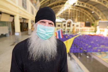 Korona virüsü salgınından korunmak için maske takan olgun sakallı turist portresi tren istasyonunda sosyal uzaklık