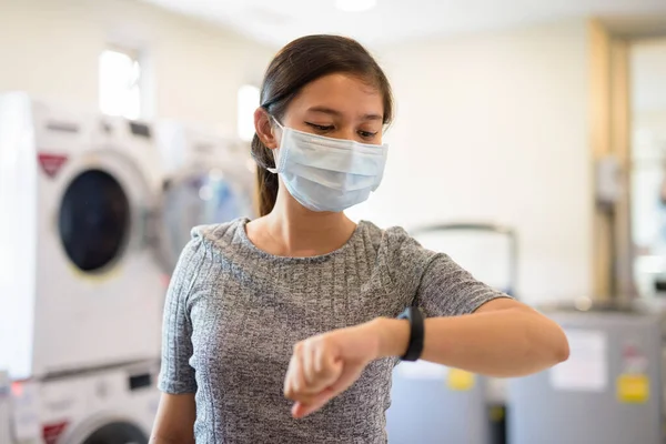 Portrait of young Filipino woman with mask for protection from corona virus outbreak at the laundromat indoors