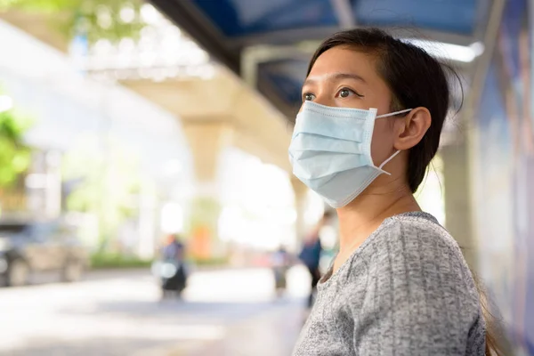 Portrait of young Filipino woman with mask for protection from corona virus outbreak at the bus stop in the city outdoors