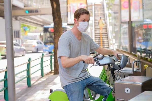 Portrait of young Scandinavian man with mask for protection from corona virus outbreak at public bicycle service station